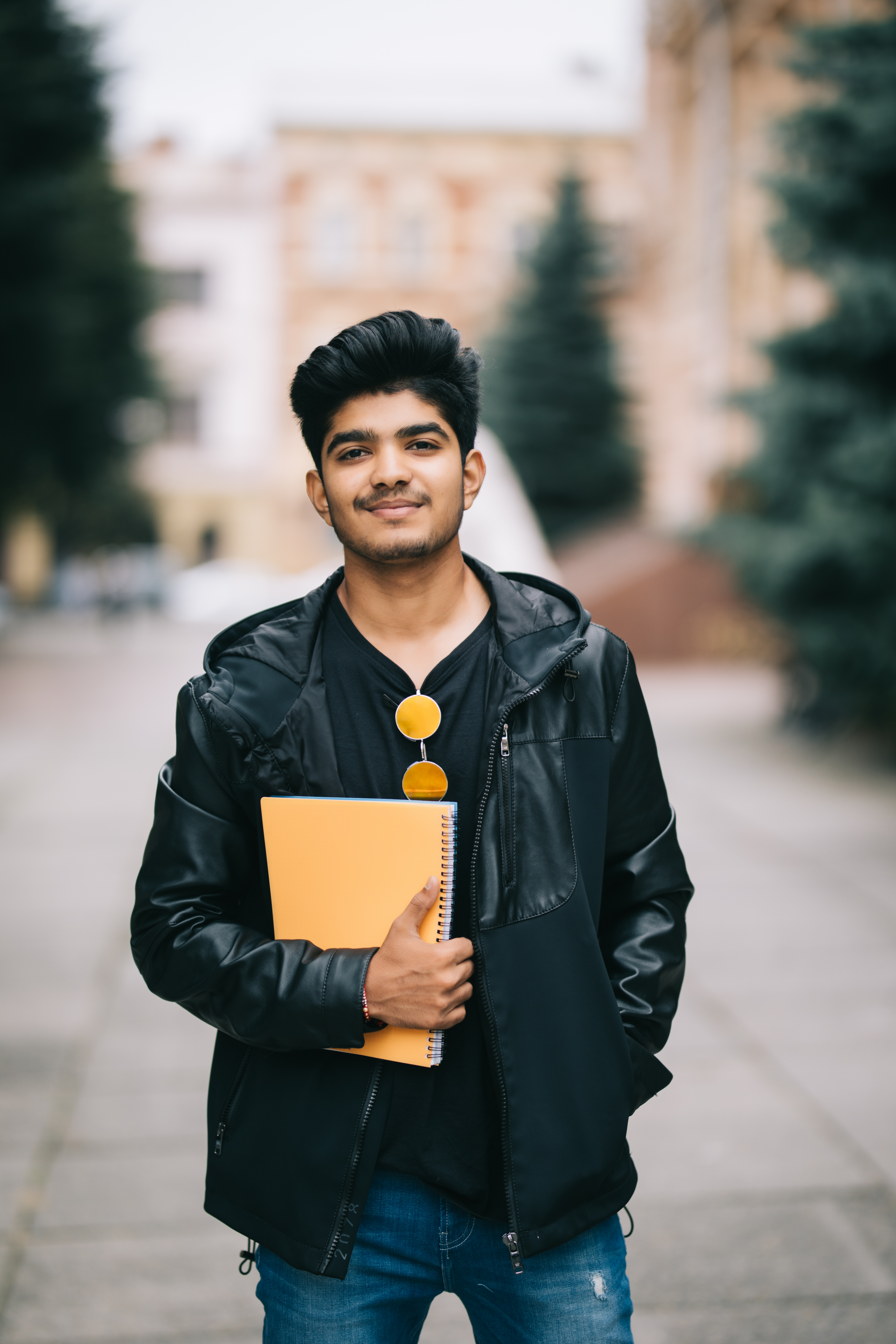 Handsome young indian student man holding notebooks while standing on the street Handsome young indian student man read notebooks while standing on the street